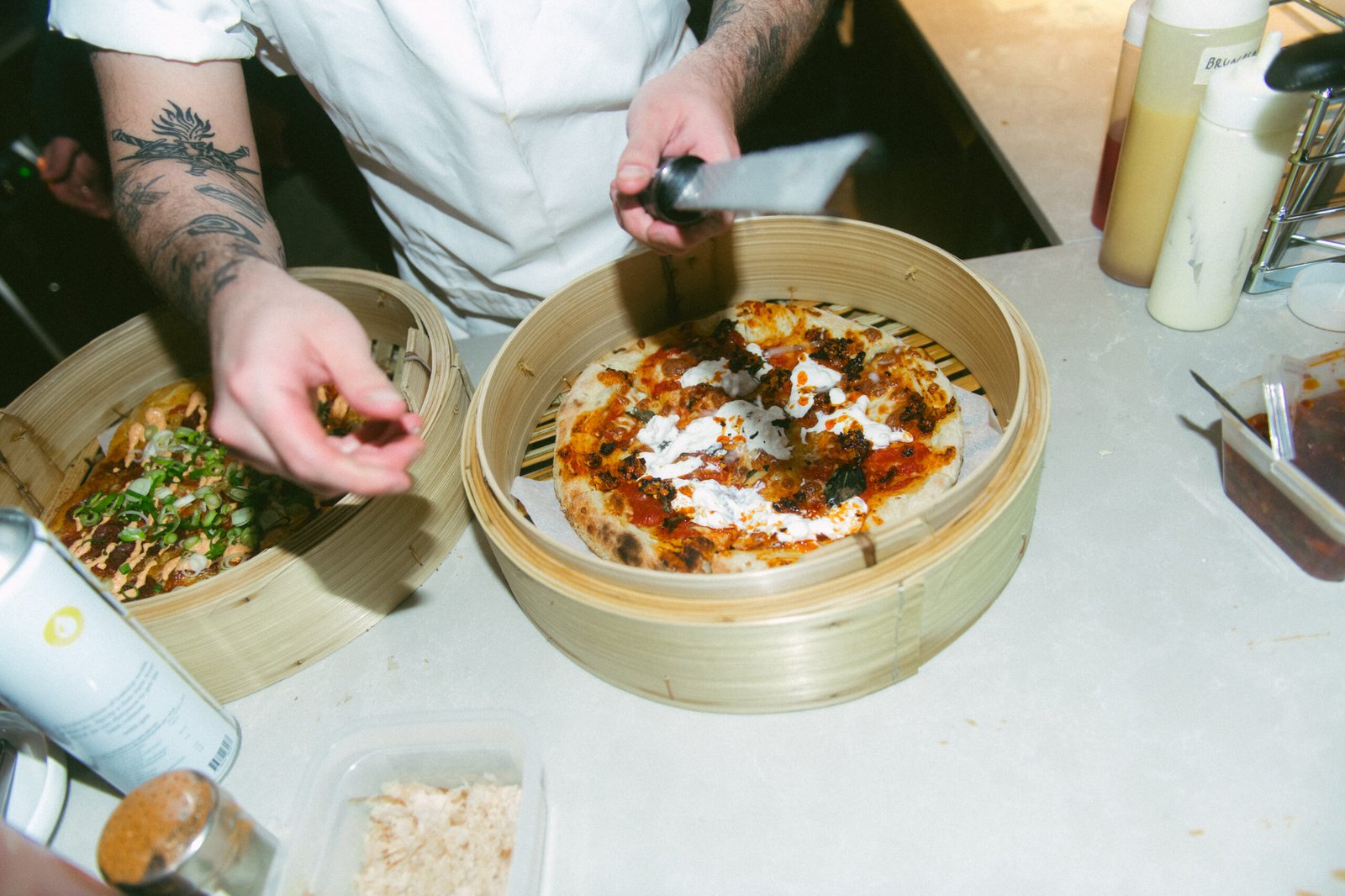 Kokk strør friske urter over en pizza servert i bambuskurv